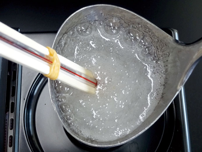 お玉に砂糖約45 g（大さじ4）と水10 mL（小さじ2）を入れ，加熱器具を用いて中火でかき混ぜながら加熱する。