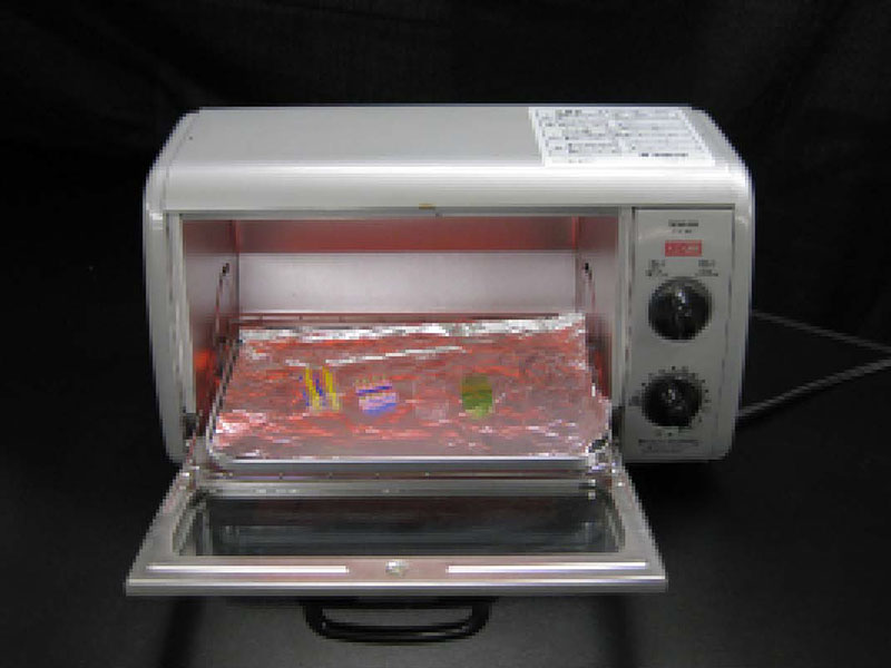 実験方法3: <strong>オーブンに入れる　オーブントースターのトレーにアルミニウム箔を敷いて，2分間予熱してから，アルミニウム箔の上にペットボトル片をペットボトルの内側だった面を上にして置き，ドアを閉めます。