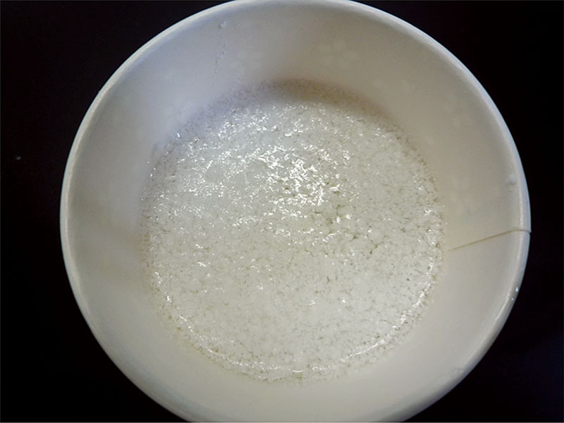 実験手順2: 20 gのクエン酸を30 mLの水に溶かす。1の石けん水が冷めたら，かき混ぜながら30 mLのクエン酸水溶液を3回程度に分けて加える。浮いてきた固形物（右の写真）をスプーンですくって，水道水を入れた別の紙コップの中に移す。
